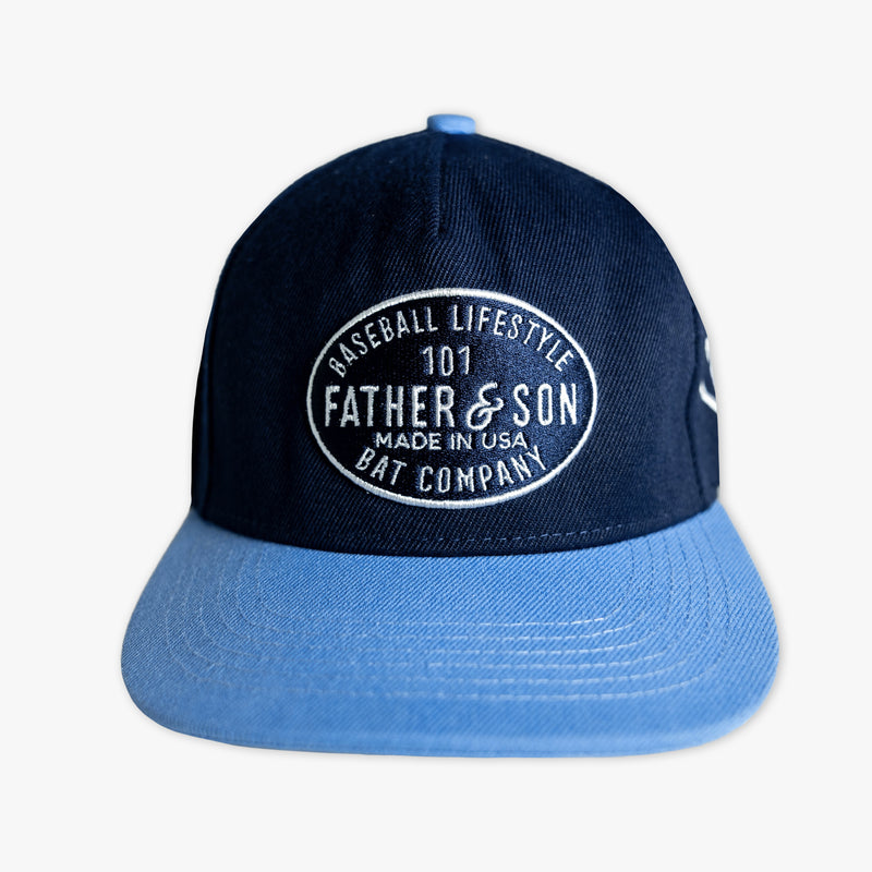 Front view of the BL101 Bat Co Snapback in navy and columbia blue featuring an embroidered Father & Son Bat Company oval patch on the crown.