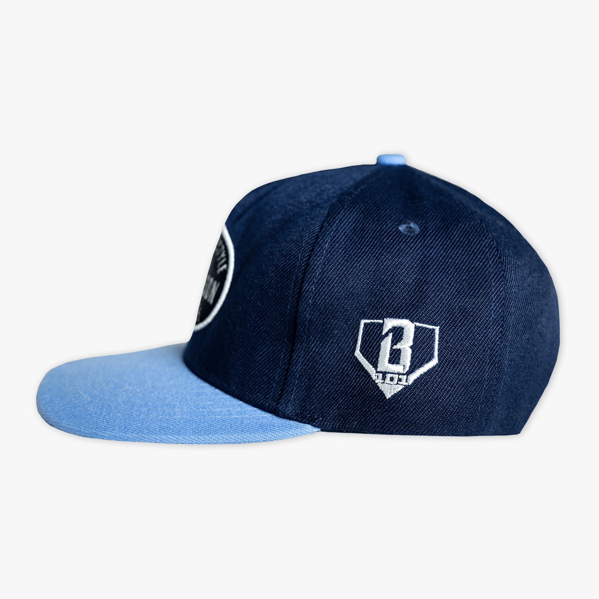 Side view of the BL101 Bat Co Snapback in navy and columbia blue showing the embroidered BL101 home plate logo on the side panel.