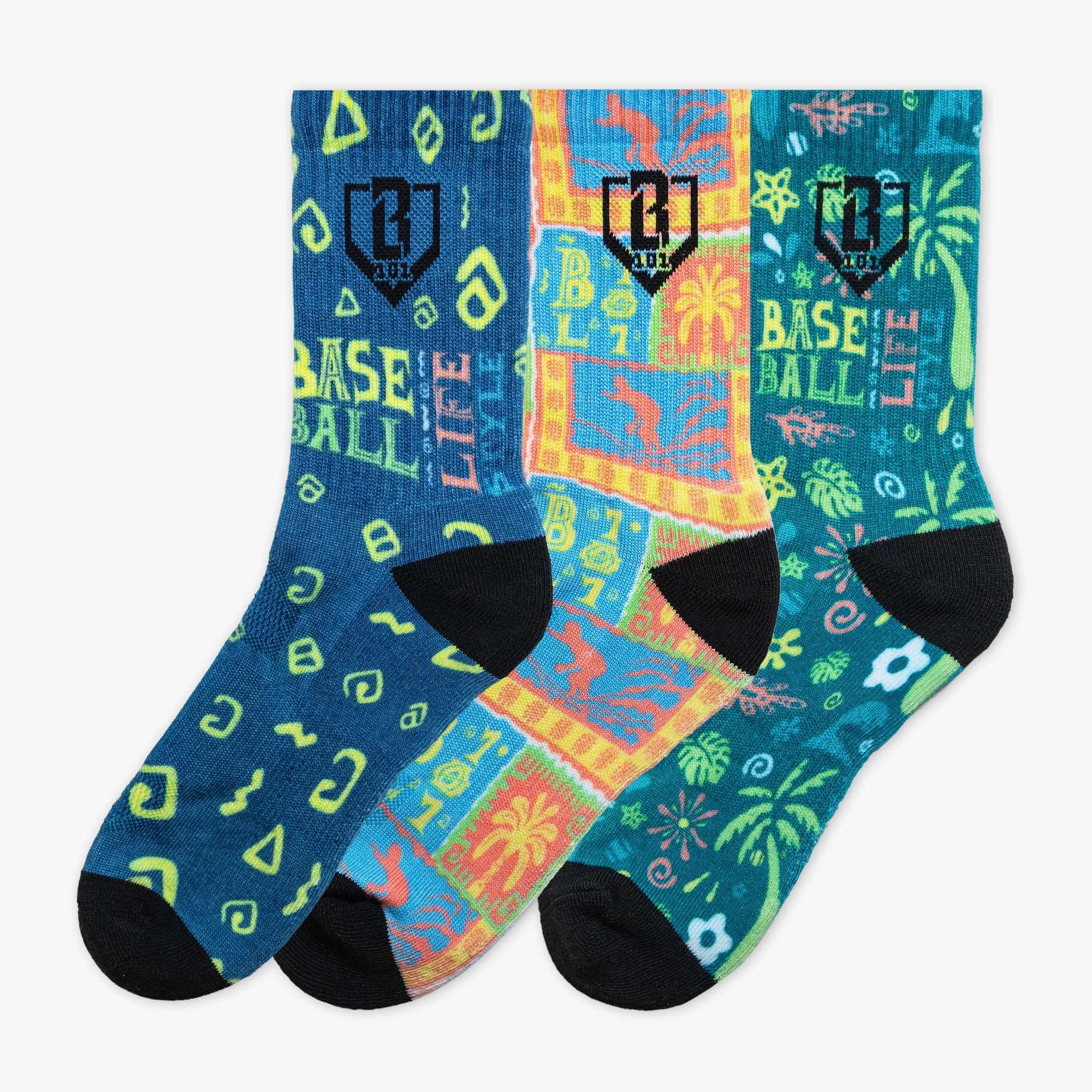 Three pairs of crew socks with colorful tropical and geometric patterns, featuring black heels, toes, and cuffs, displayed against a plain white background.