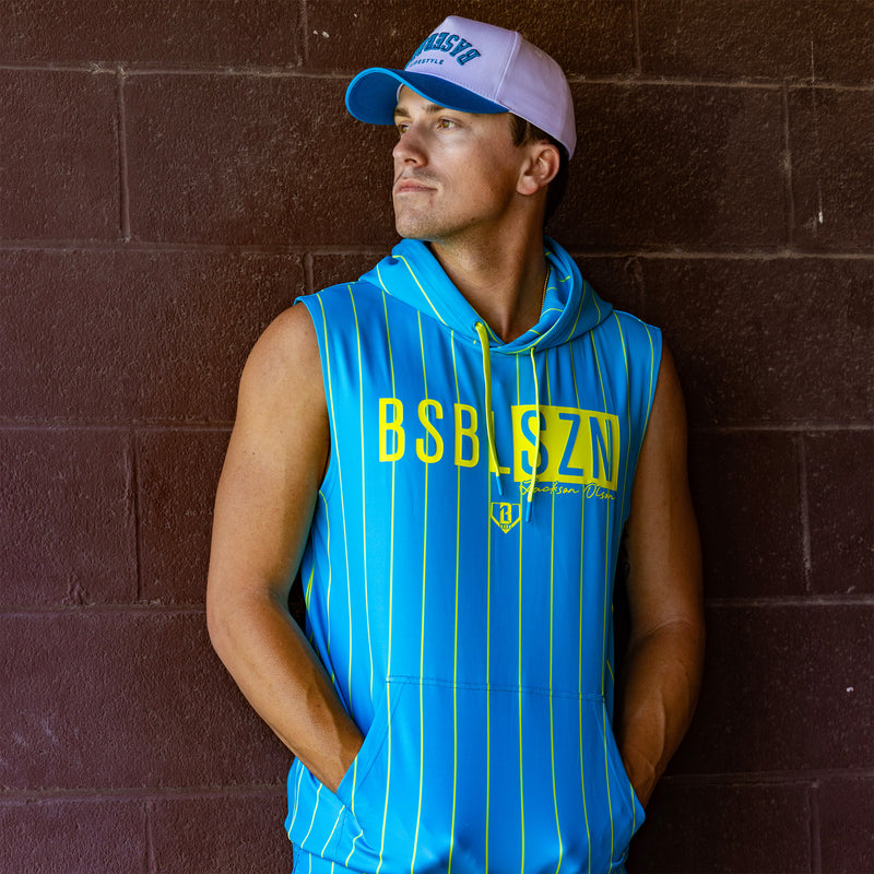 Man wearing a blue sleeveless hoodie with yellow stripes and 'BSBLSZN Jackson Olson' text against a brick wall