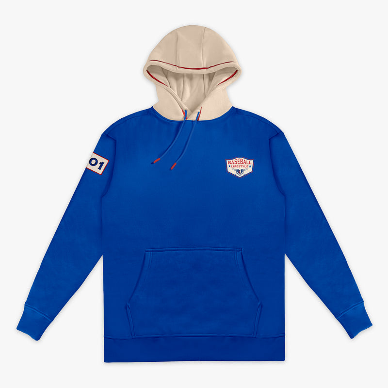 Royal blue hoodie with a cream hood, showing the Baseball Lifestyle shield chest logo, sleeve patch, and red drawstring on a white background.