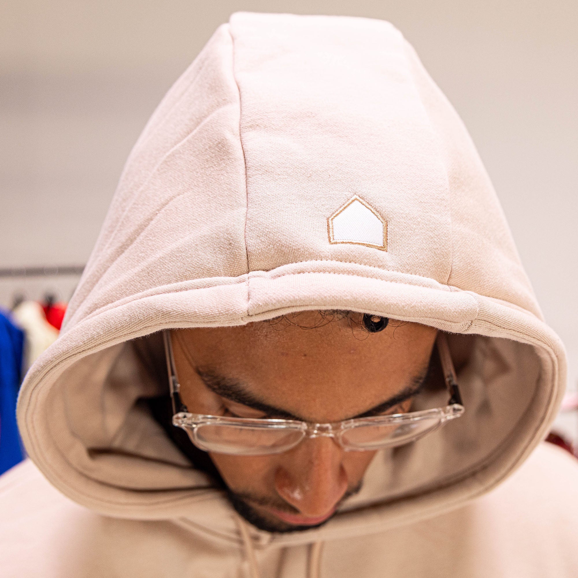 Person wearing a beige hoodie with a small logo, looking downwards.