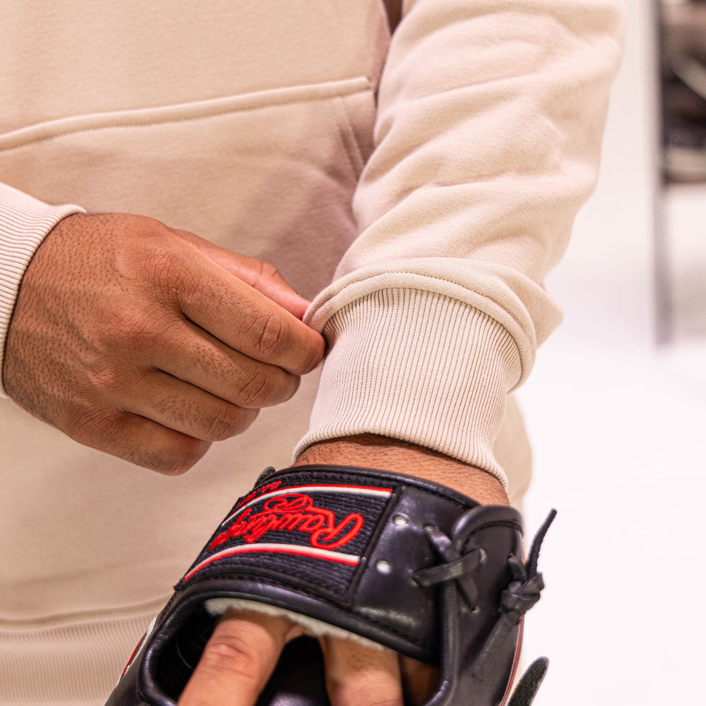 Person wearing a beige sweatshirt with a black baseball glove featuring red text on the wrist.