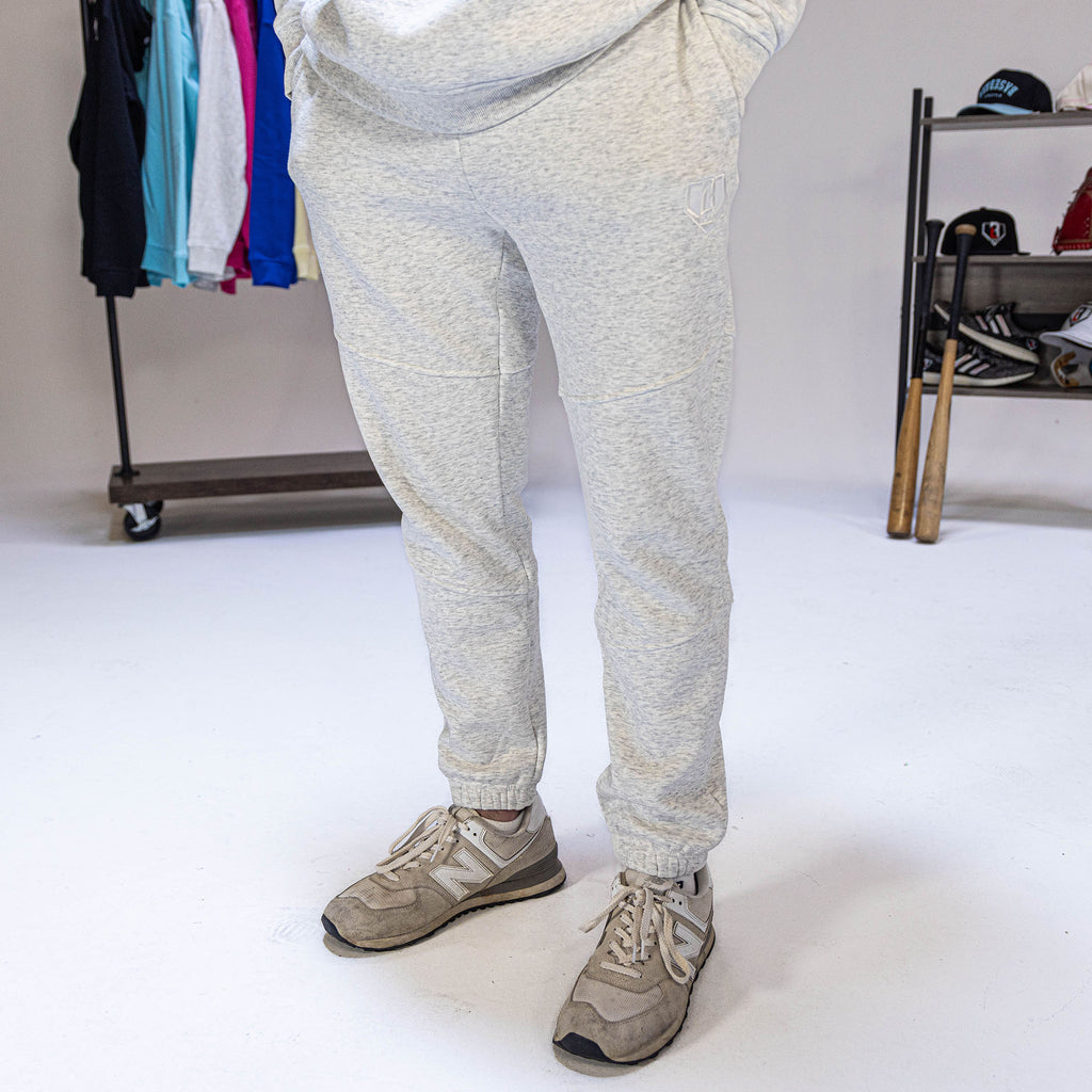 Person wearing light gray sweatpants with a BL101 logo on a white background with clothing items in the background.