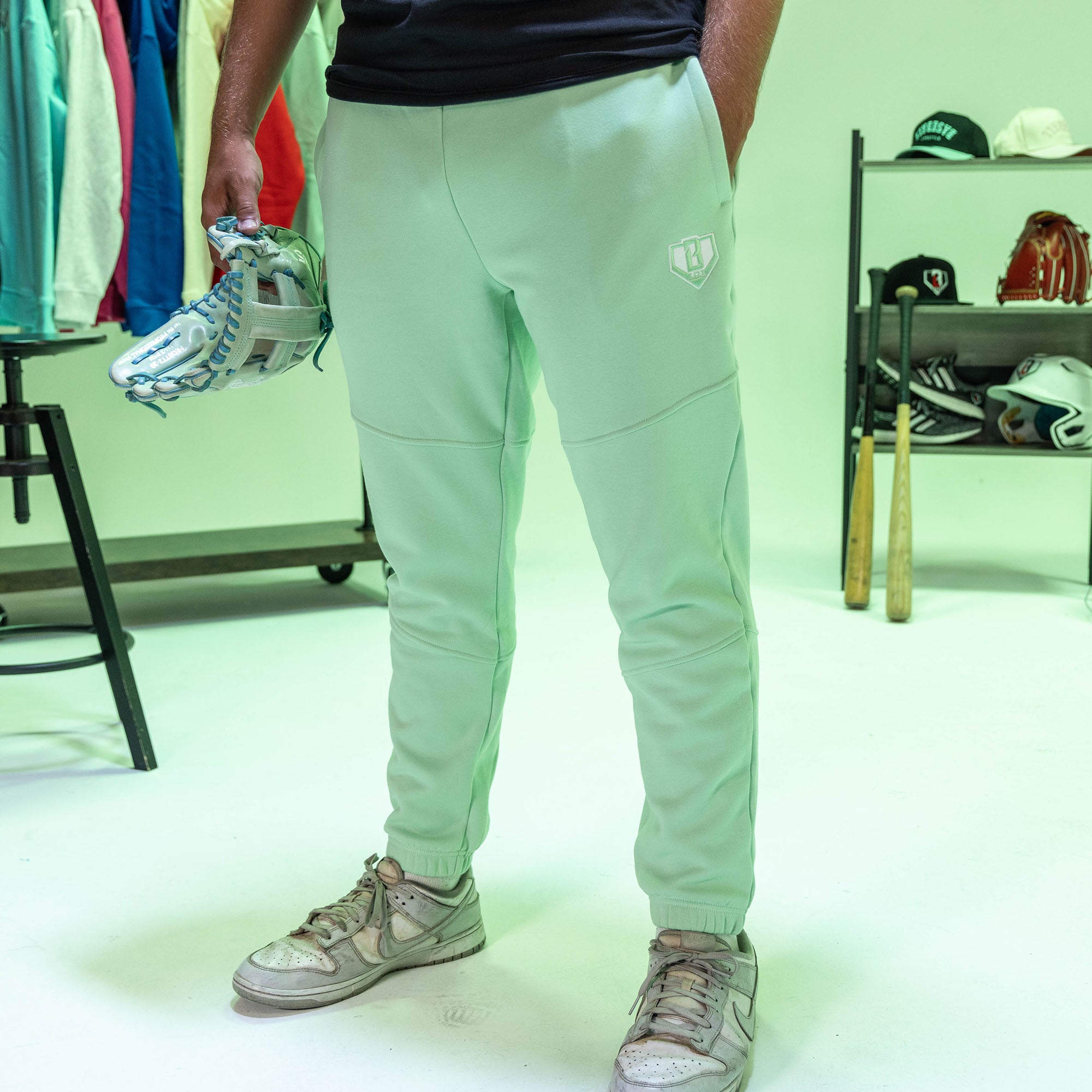 Person wearing light green jogger pants with a white BL101 logo, holding sports equipment in a room with sports equipment in the background.