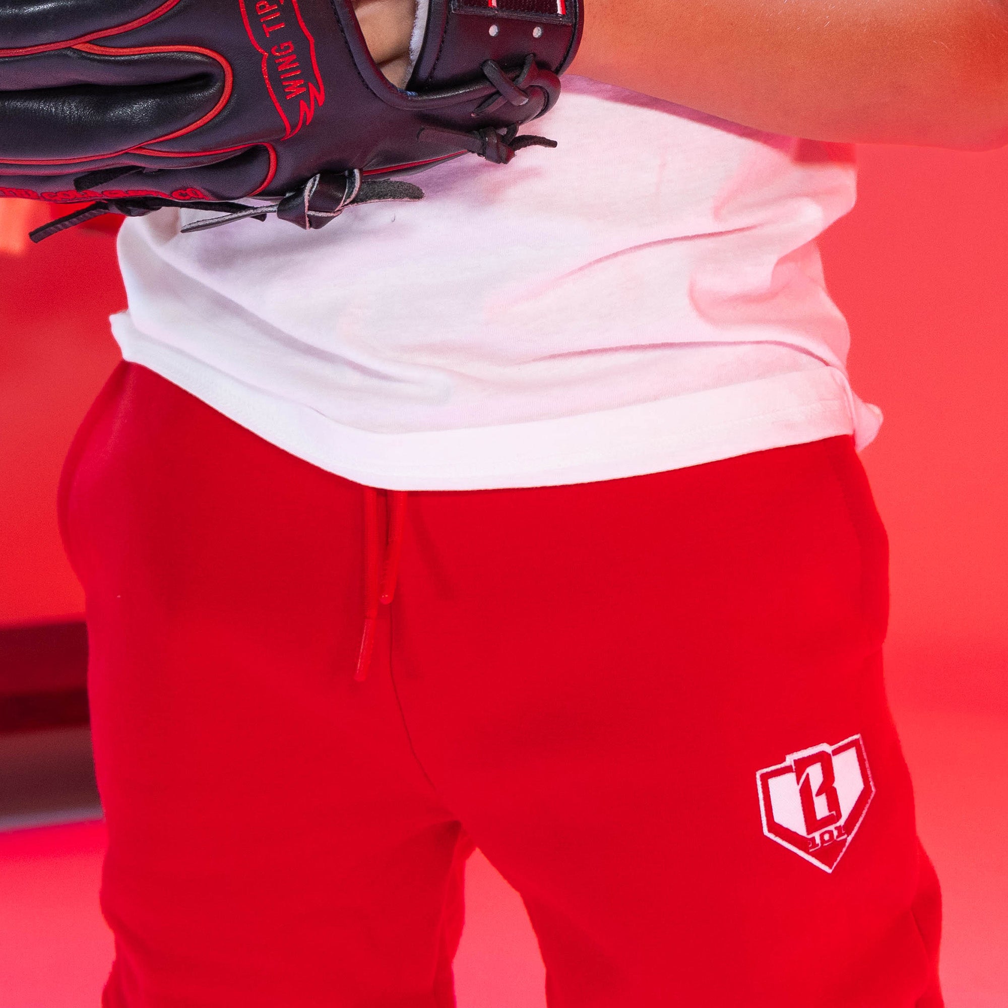 Person wearing red sweatpants with a white BL101 logo and a white shirt, holding a baseball glove against a red background.