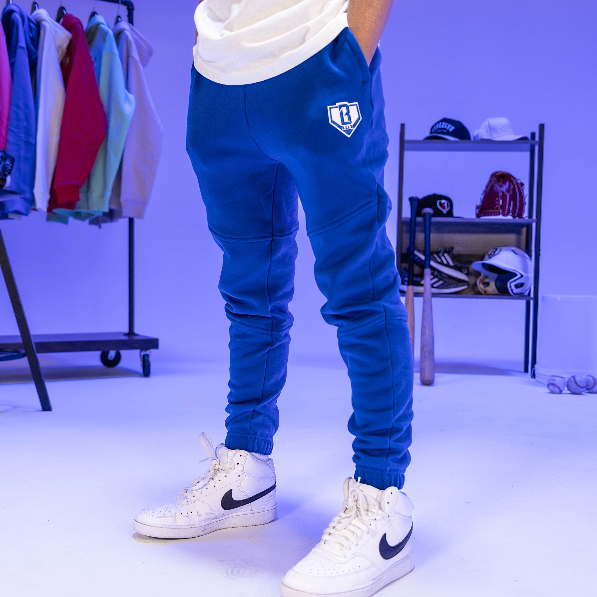 Person wearing blue pants with a BL101 logo and white sneakers in a clothing store setting.
