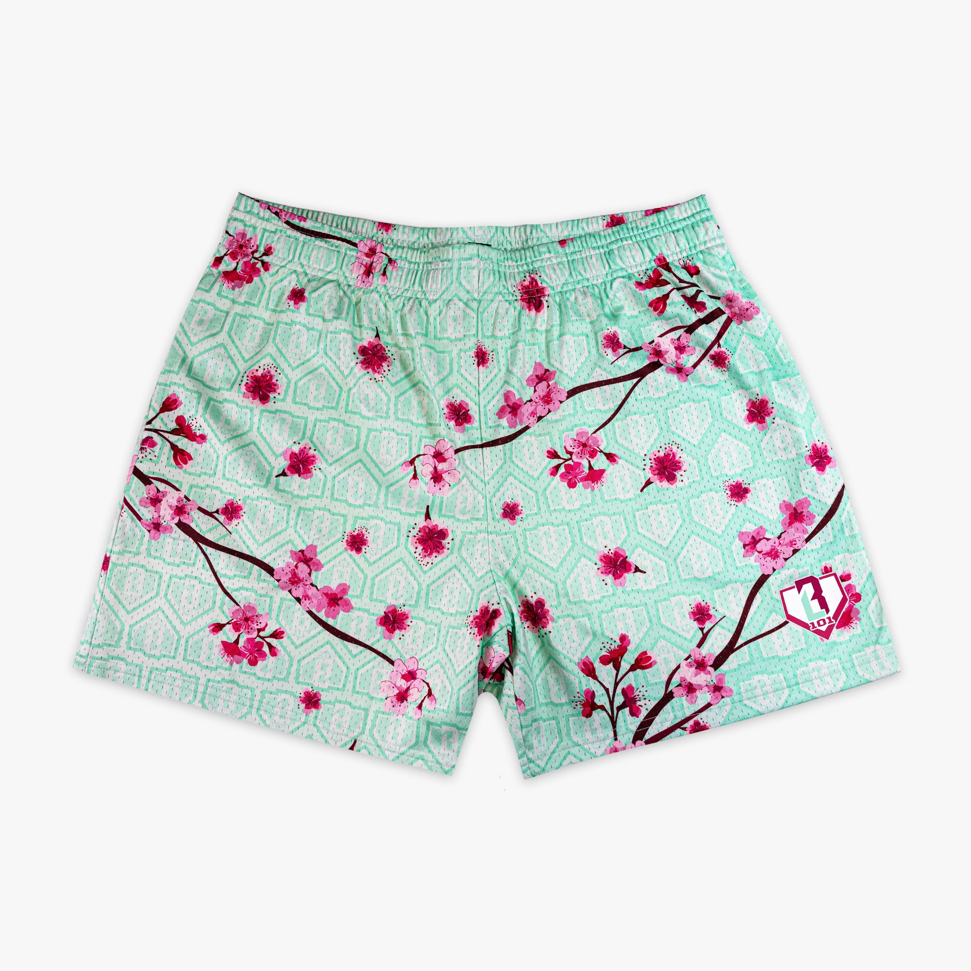 Mint green BL101 mesh shorts with a pink cherry blossom branch print over a home plate pattern background and BL101 shield logo on the right leg, flat lay front view