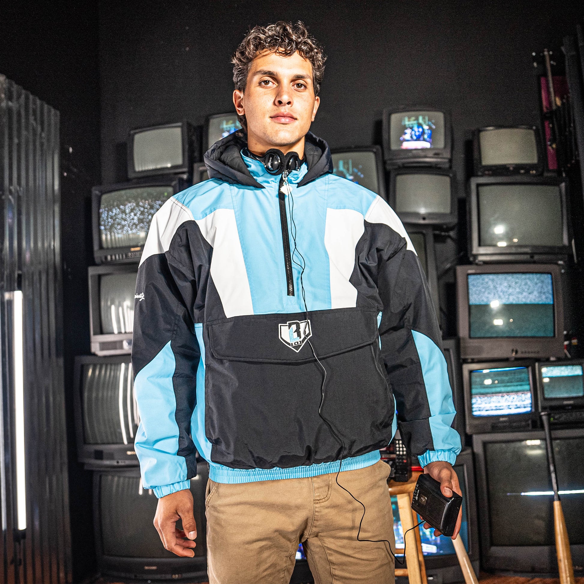 Person wearing a Blue, white and black jacket standing in front of vintage TVs.
