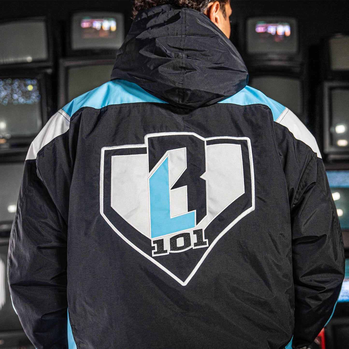 Person wearing a blue, black and white jacket with a BL101 logo on the back, standing in front of vintage arcade machines.
