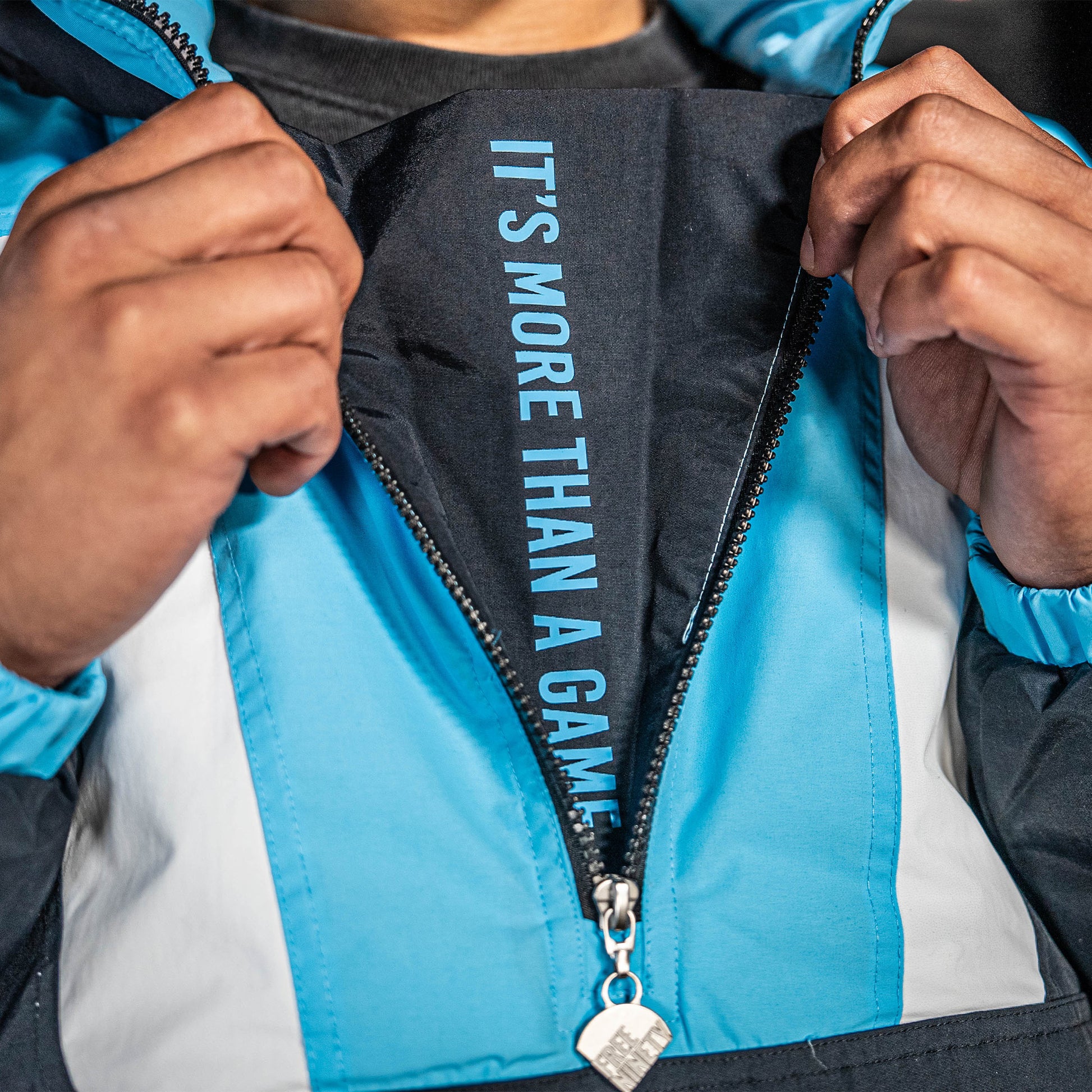 Person wearing a blue, white and black jacket with 'It's More Than A Game' text on the zipper.