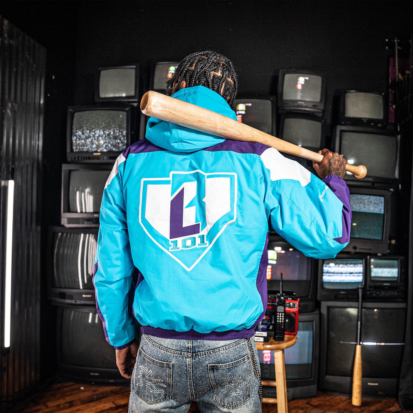Person wearing a blue, purple and white jacket with a BL101 logo in a room with multiple vintage TVs.