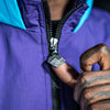 Close-up of a person wearing a purple jacket with a 'FREE NINETY' logo on the zipper, focusing on the hand and jacket.