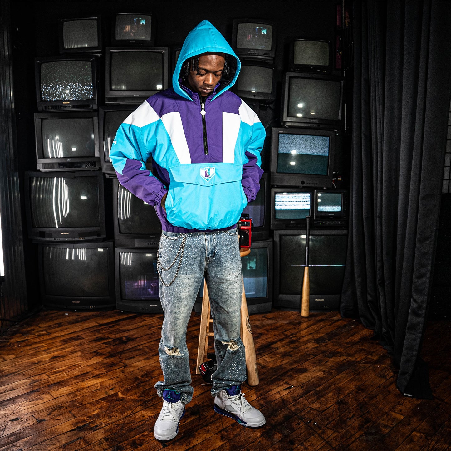Person wearing a blue, purple and white jacket with a BL101 logo in a room with multiple vintage TVs.