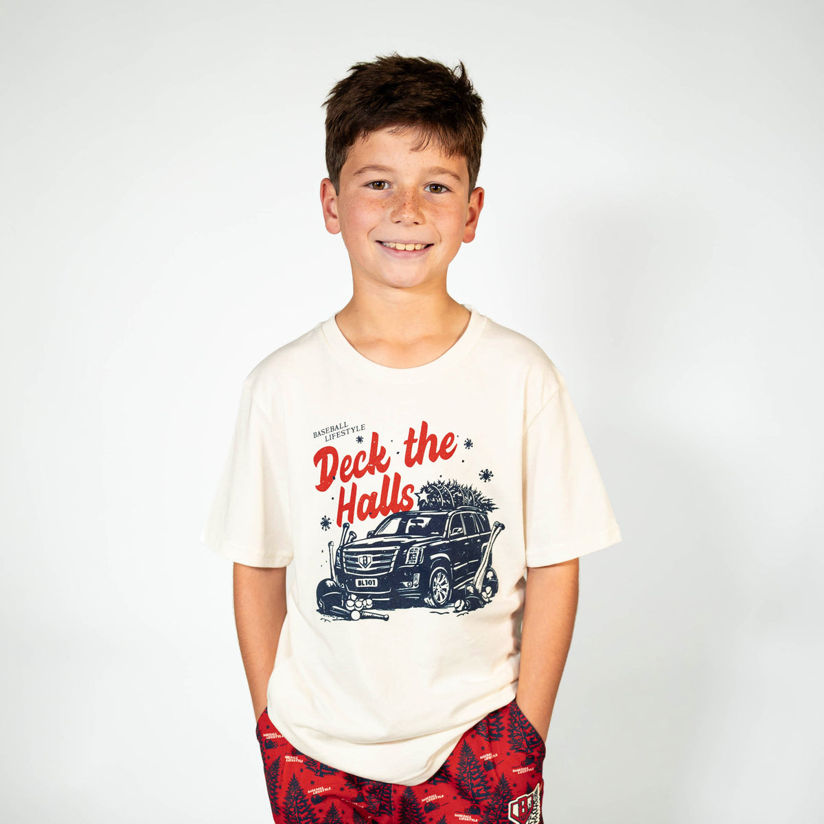 Youth model wearing white youth graphic tee with "Deck The Halls" design
