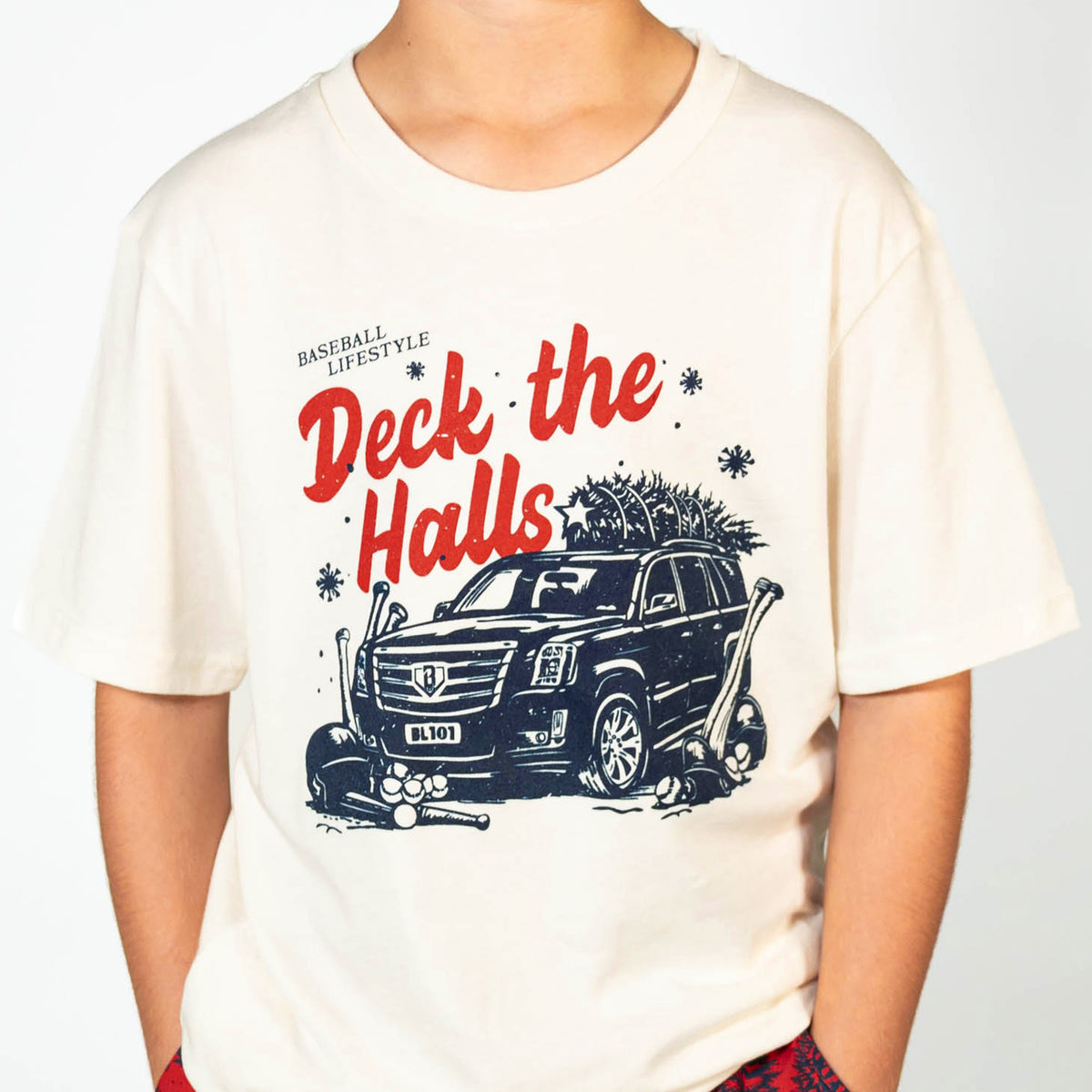 Youth model wearing white youth graphic tee with "Deck The Halls" design