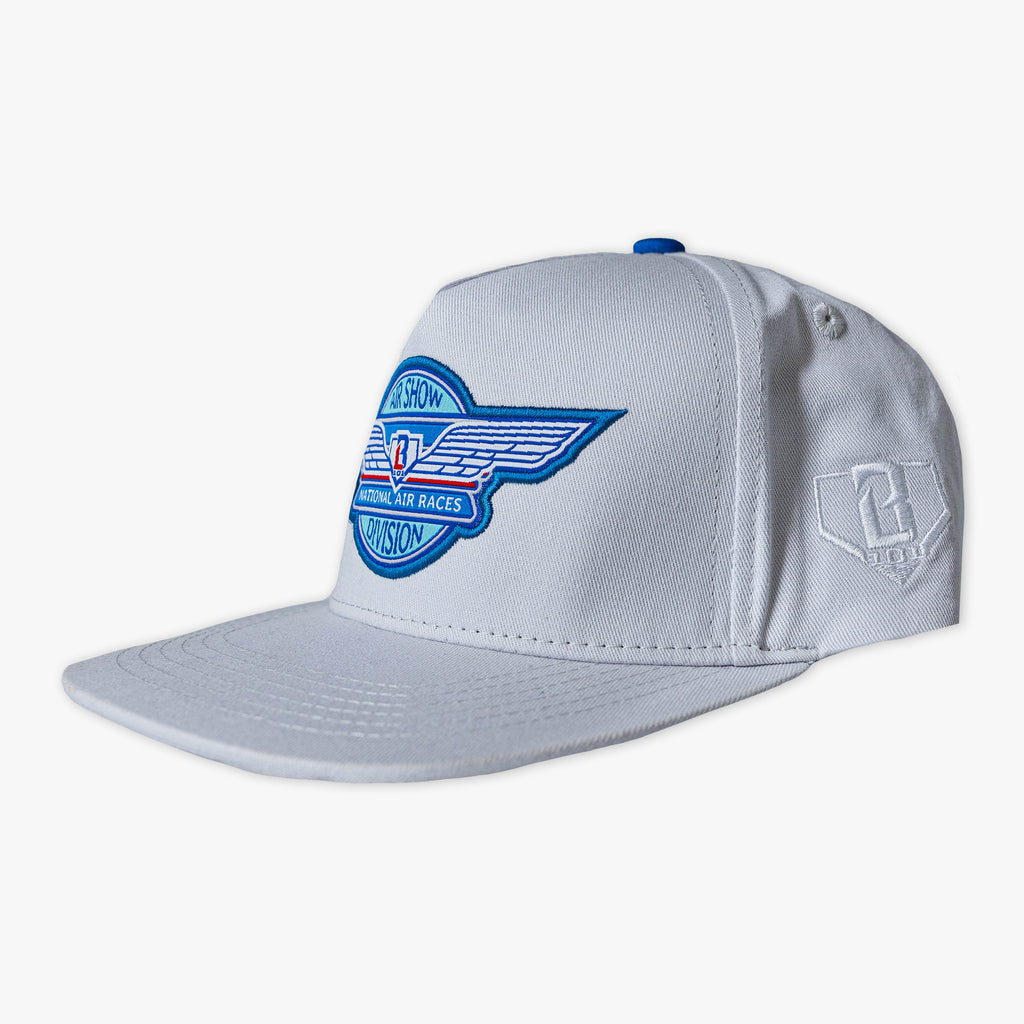 Front angle view of gray snapback hat with winged Air Show National Air Races Division embroidered patch on front panel and tonal BL101 logo embroidery on side panel on white background