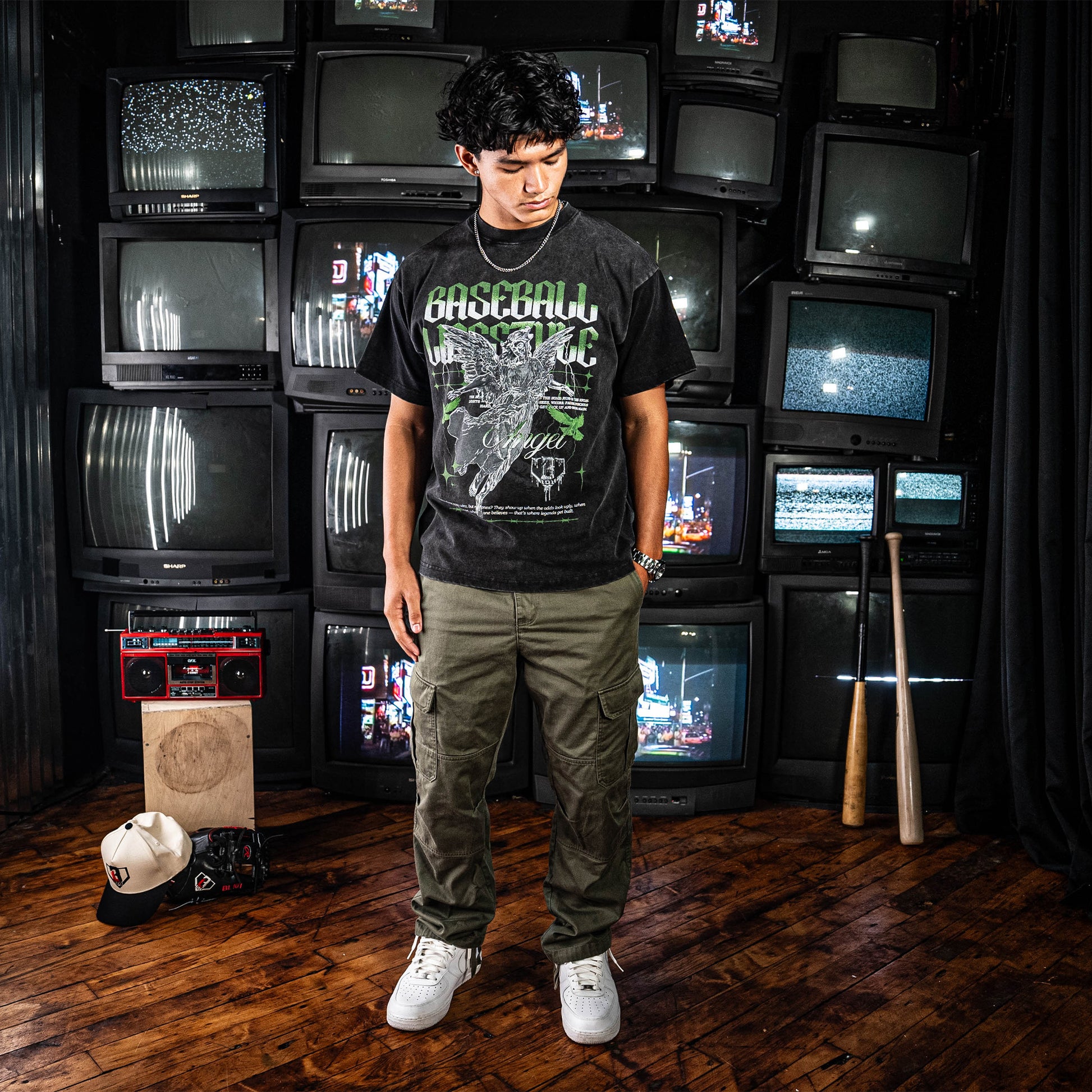 Person wearing a black t-shirt with green and white graphic design in front of stacked vintage TVs.