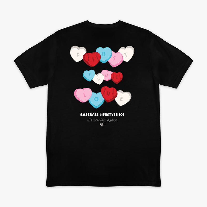 Black t-shirt with colorful heart designs and 'First True Love Baseball Lifestyle 101' text on a white background