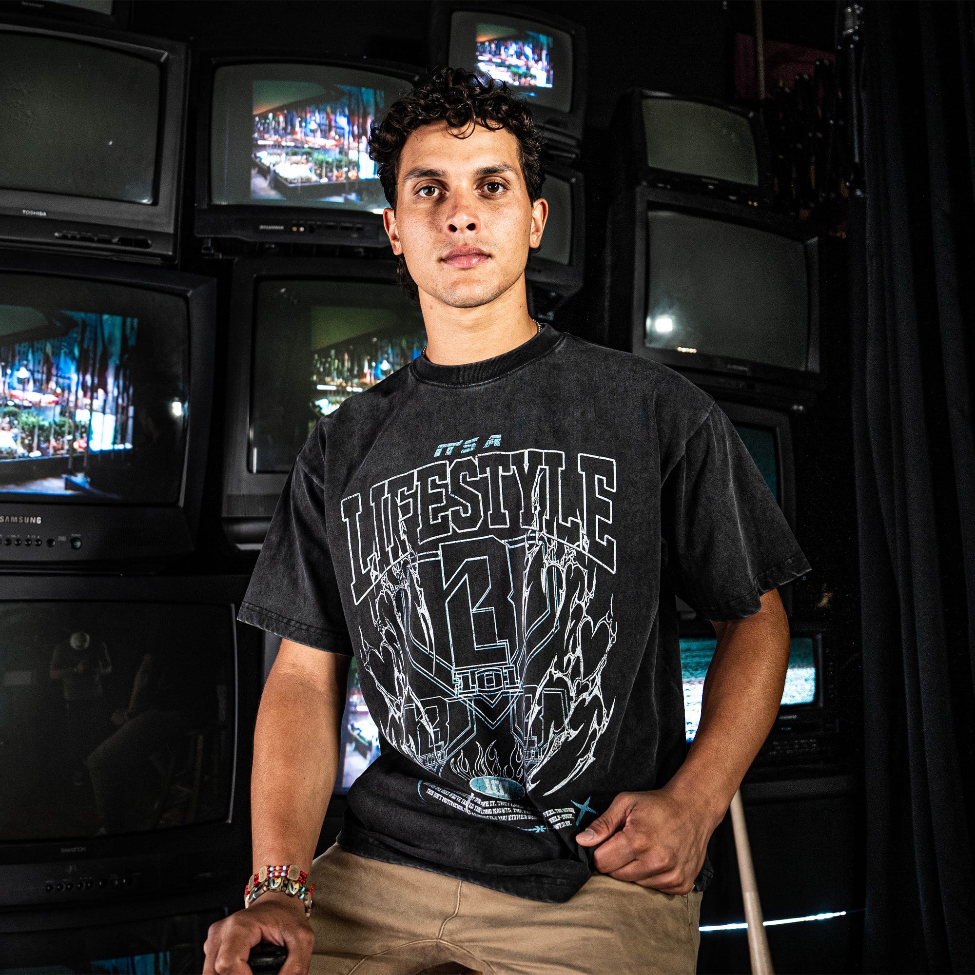Man wearing a black t-shirt with text standing in front of stacked televisions.