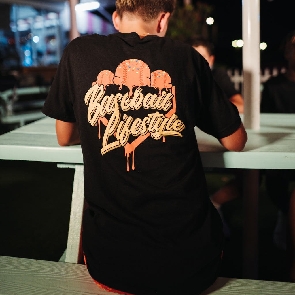 Person wearing a black t-shirt with 'Baseball Lifestyle' ice cream text at an outdoor setting