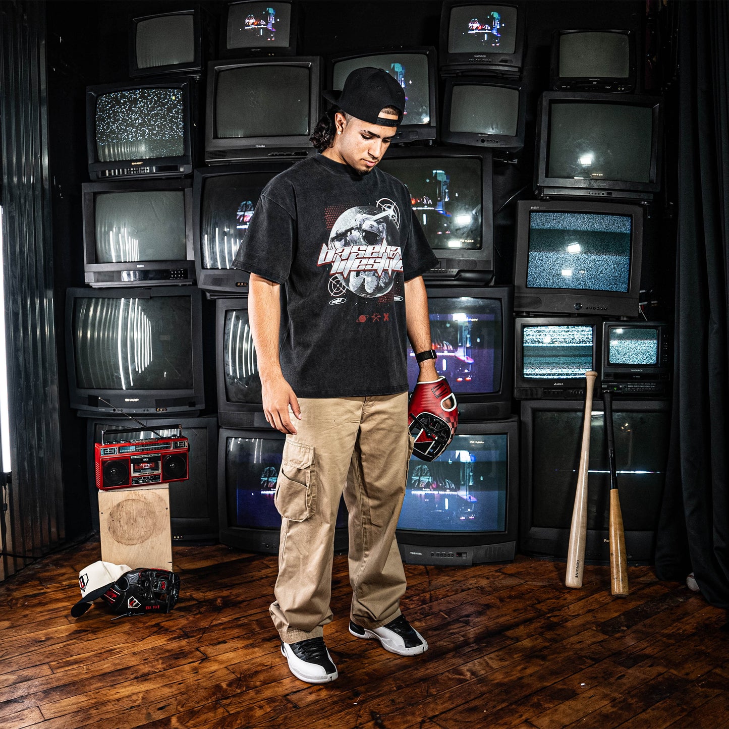 Person wearing a black t-shirt with a graphic design, standing in front of a wall of vintage televisions.