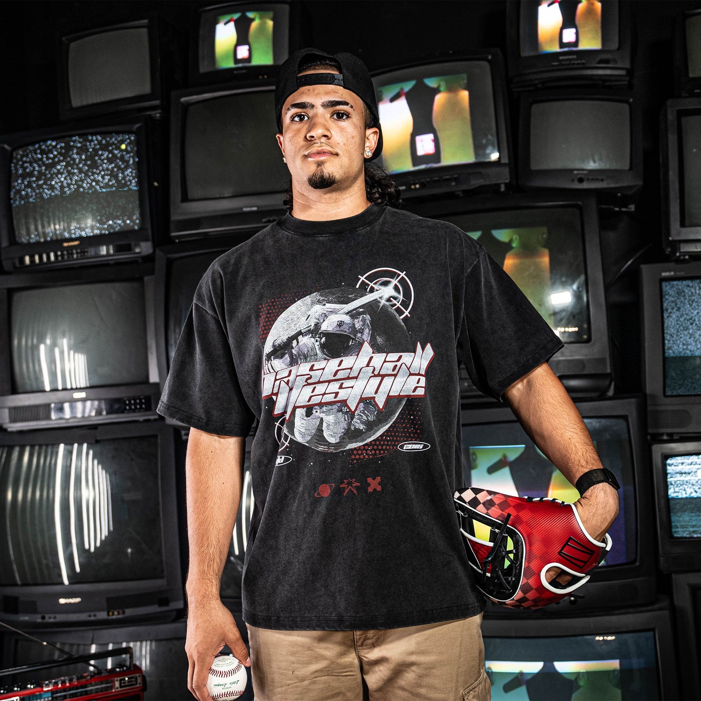 Man wearing a black t-shirt with graphic design and 'Baseball Lifestyle' text in front of vintage televisions