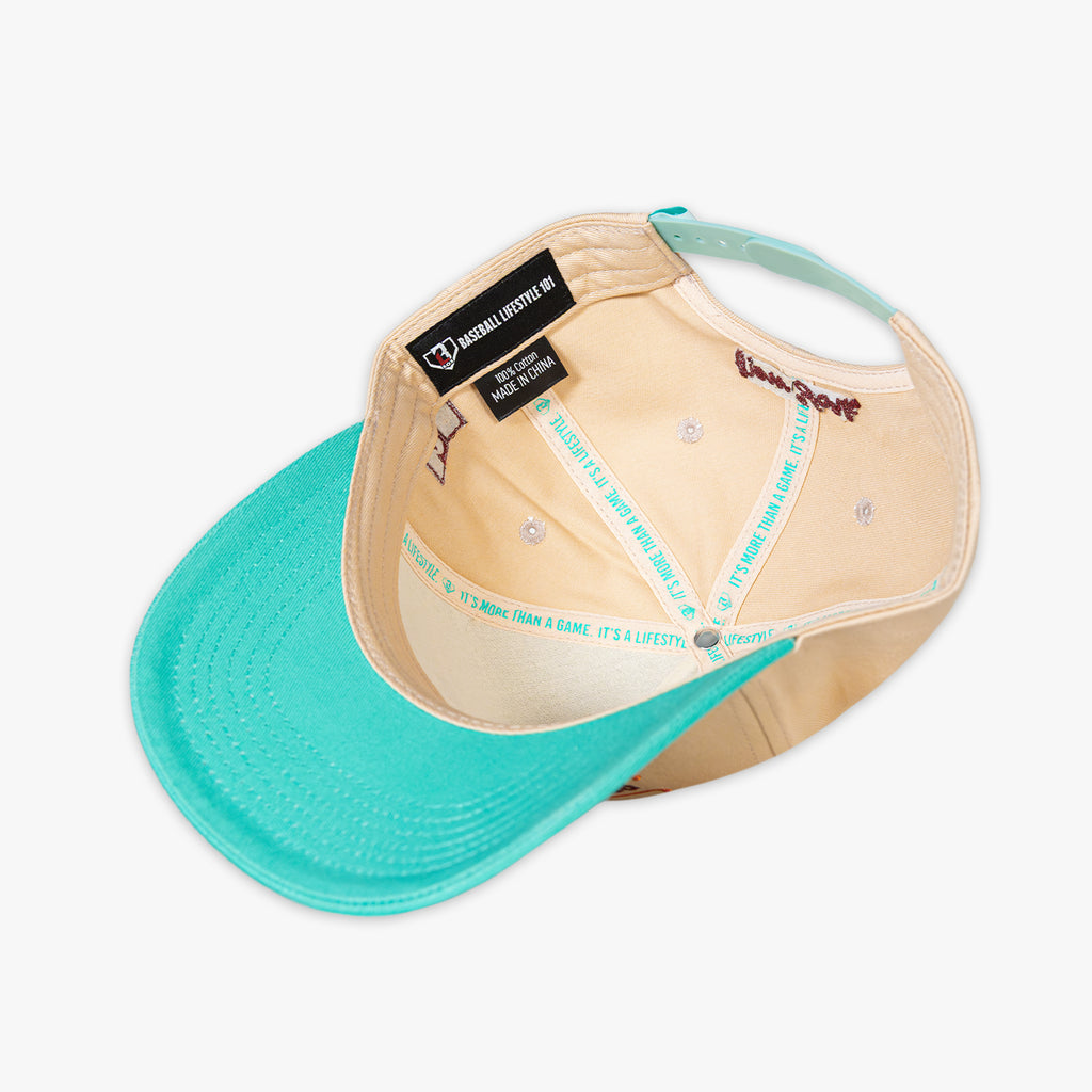 Beige and teal baseball cap with a brand label on a white background