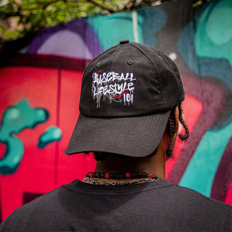 Person wearing a black cap with white and red 'Baseball Lifestyle 101' text against a colorful graffiti background