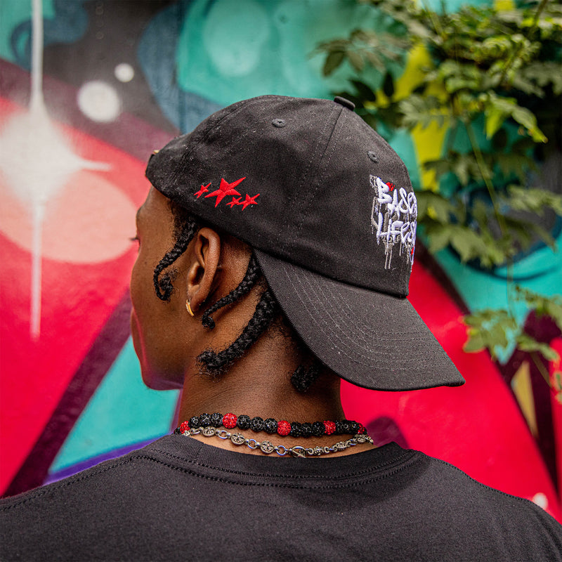 Person wearing a black cap with 'Baseball Lifestyle 101' text and star graphics, standing in front of a colorful mural.