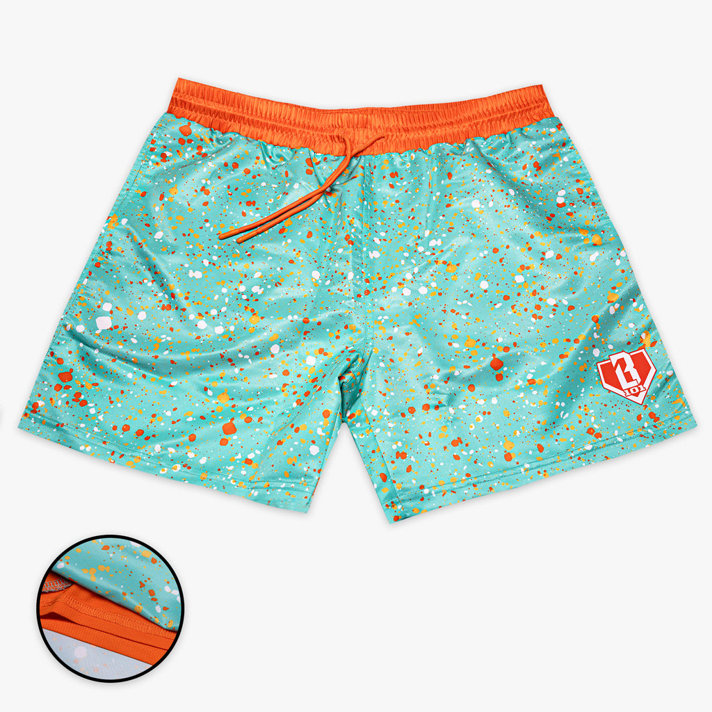 Front flat lay of BL101 teal splatter print swim trunks with an orange waistband and drawstring, BL101 logo on the leg, and a liner detail inset.