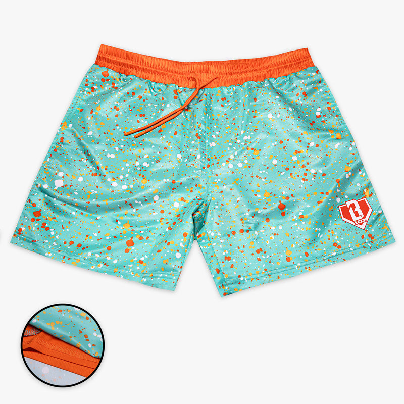 Front flat lay of BL101 teal splatter print swim trunks with an orange waistband and drawstring, BL101 logo on the leg, and a liner detail inset.