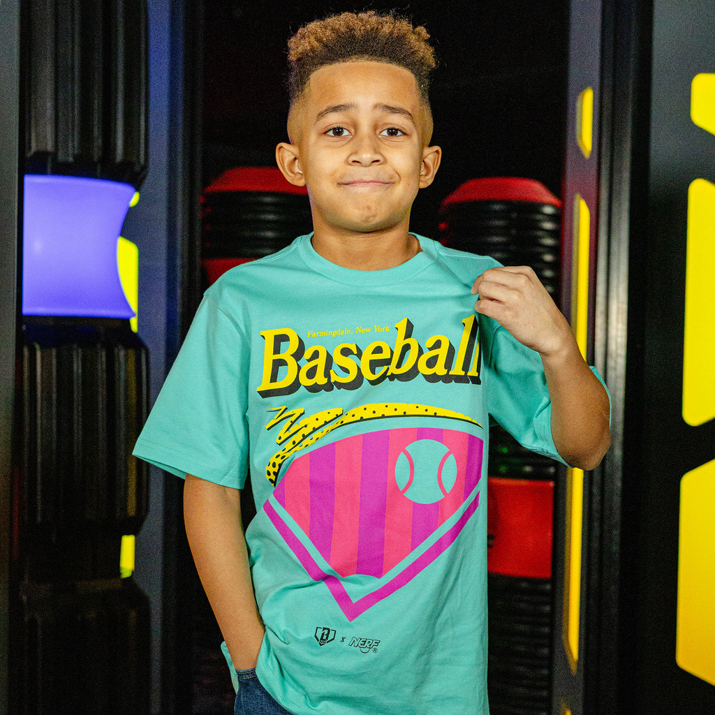 Child wearing a teal t-shirt with a colorful 'Baseball' design and 'BL101 X NERF' logo, standing in front of a colorful design.