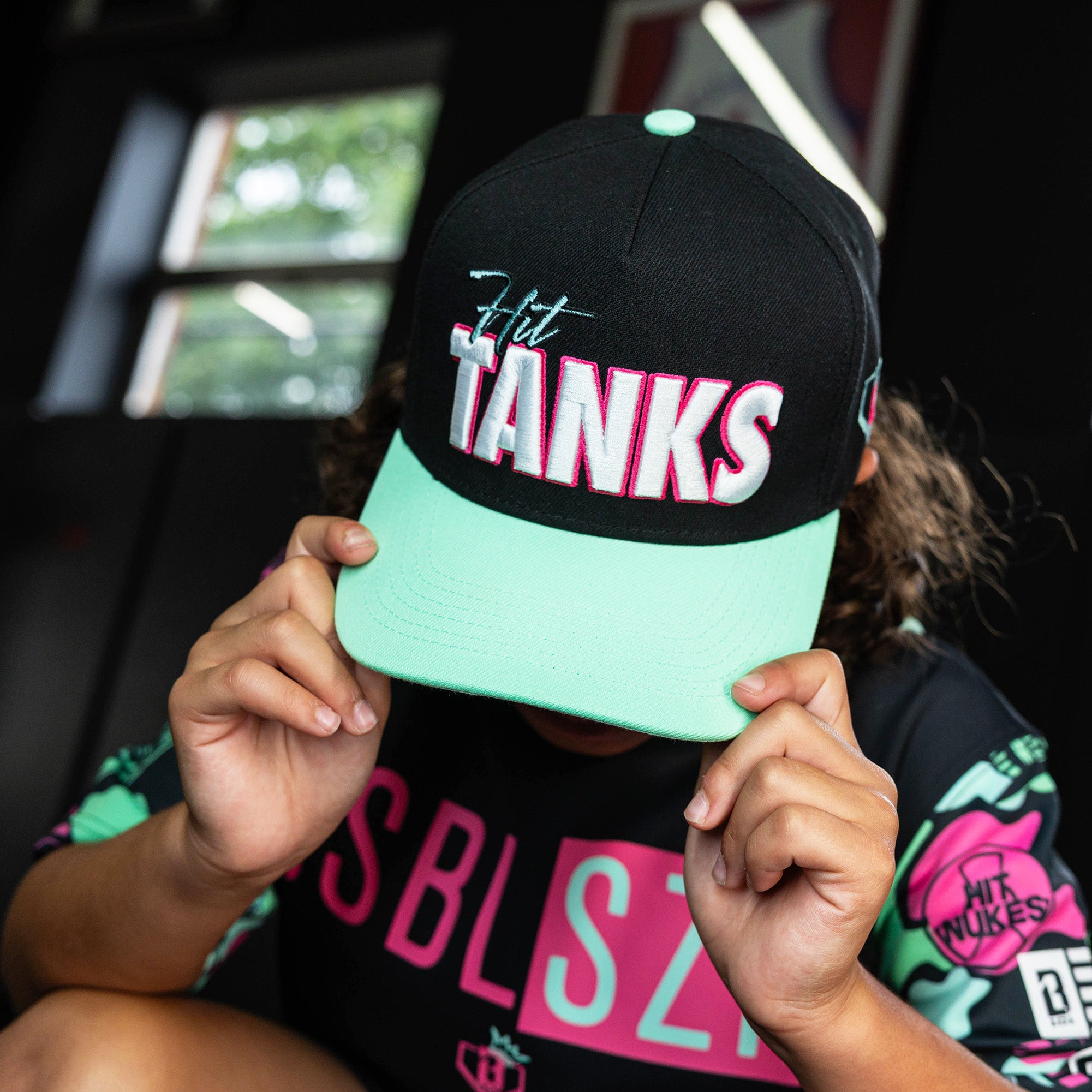 Youth model wearing black hat with "Hit Tanks" design