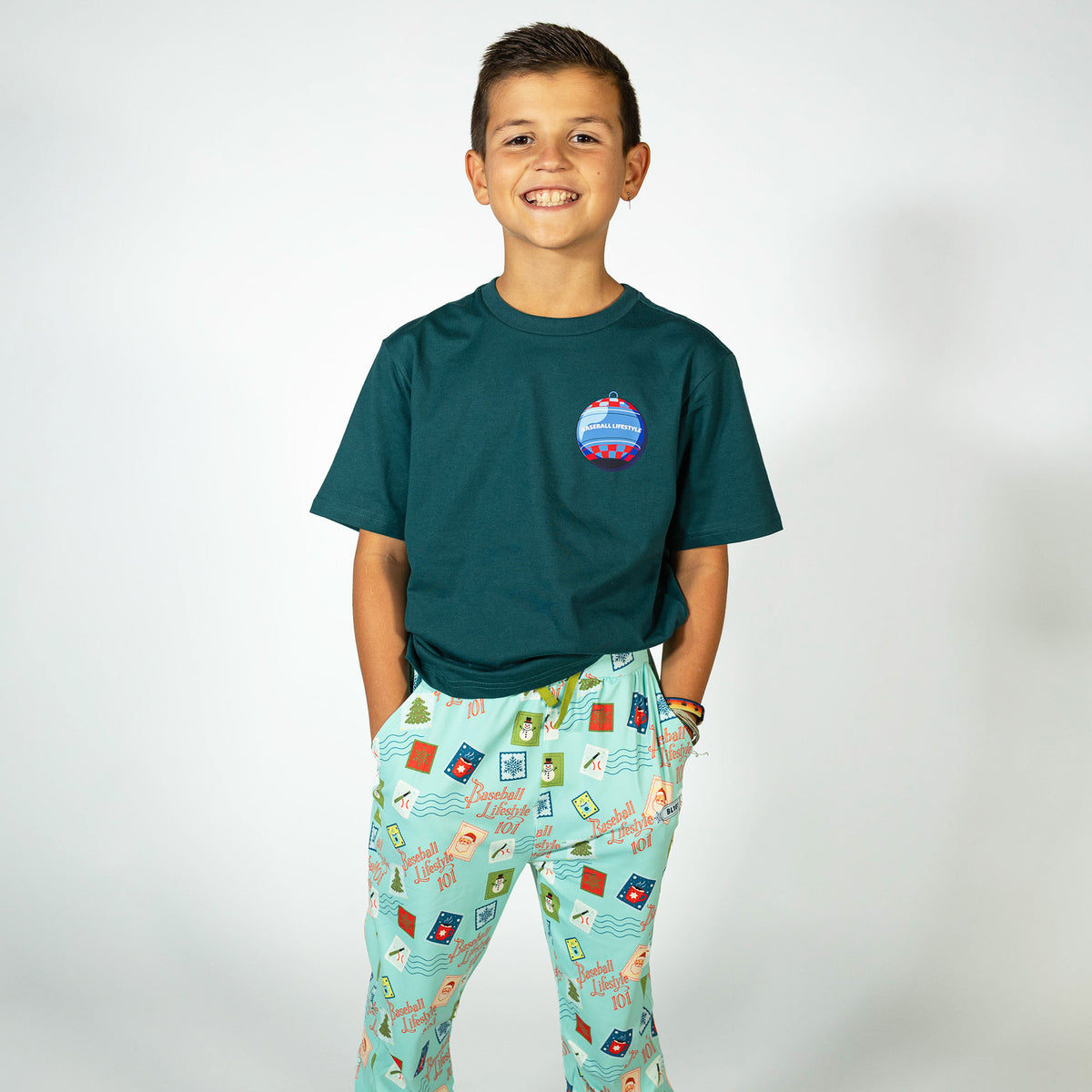 Youth model wearing teal youth pajama pants with "Holiday Stamps" design