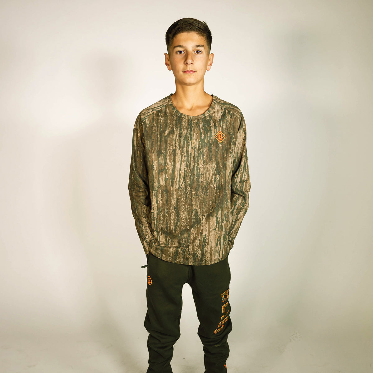 Youth model wearing multi-color Realtree Legacy Diamond Tech Camo youth long sleeve