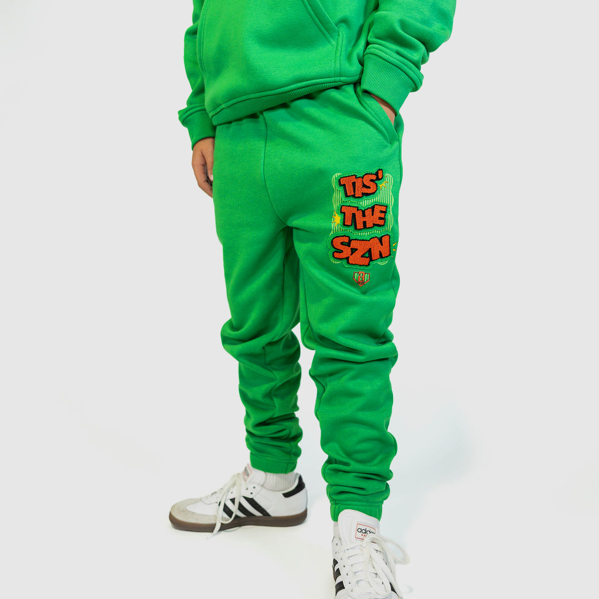 Youth model wearing green youth sweatpants with "Tis The SZN" design