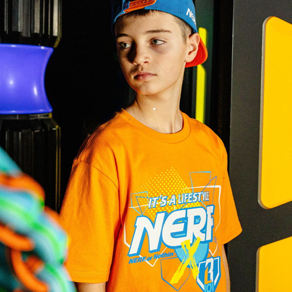Child wearing an orange 'NERF X BL101' t-shirt with a blue cap in a colorful setting