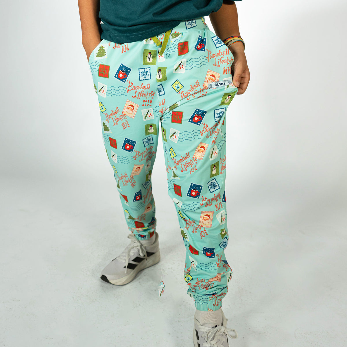 Youth model wearing teal youth pajama pants with "Holiday Stamps" design
