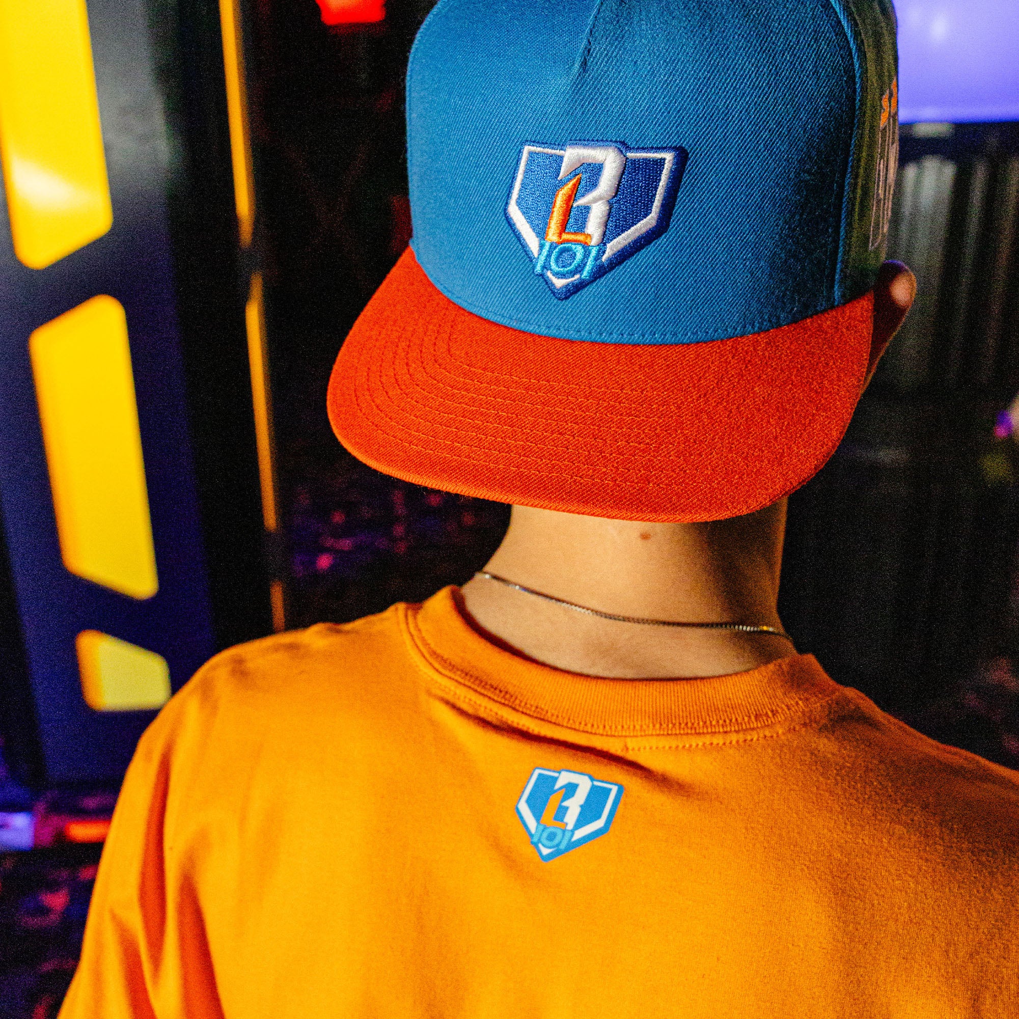 Person wearing a blue and red BL101 cap, standing in front of colorful lights.