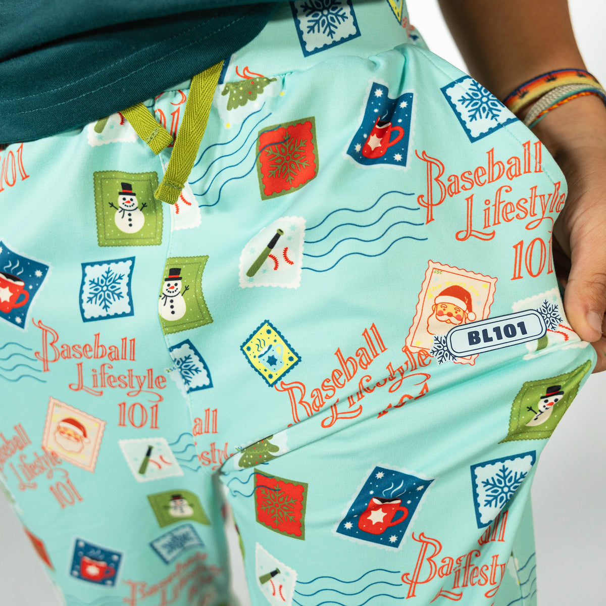 Youth model wearing teal youth pajama pants with "Holiday Stamps" design