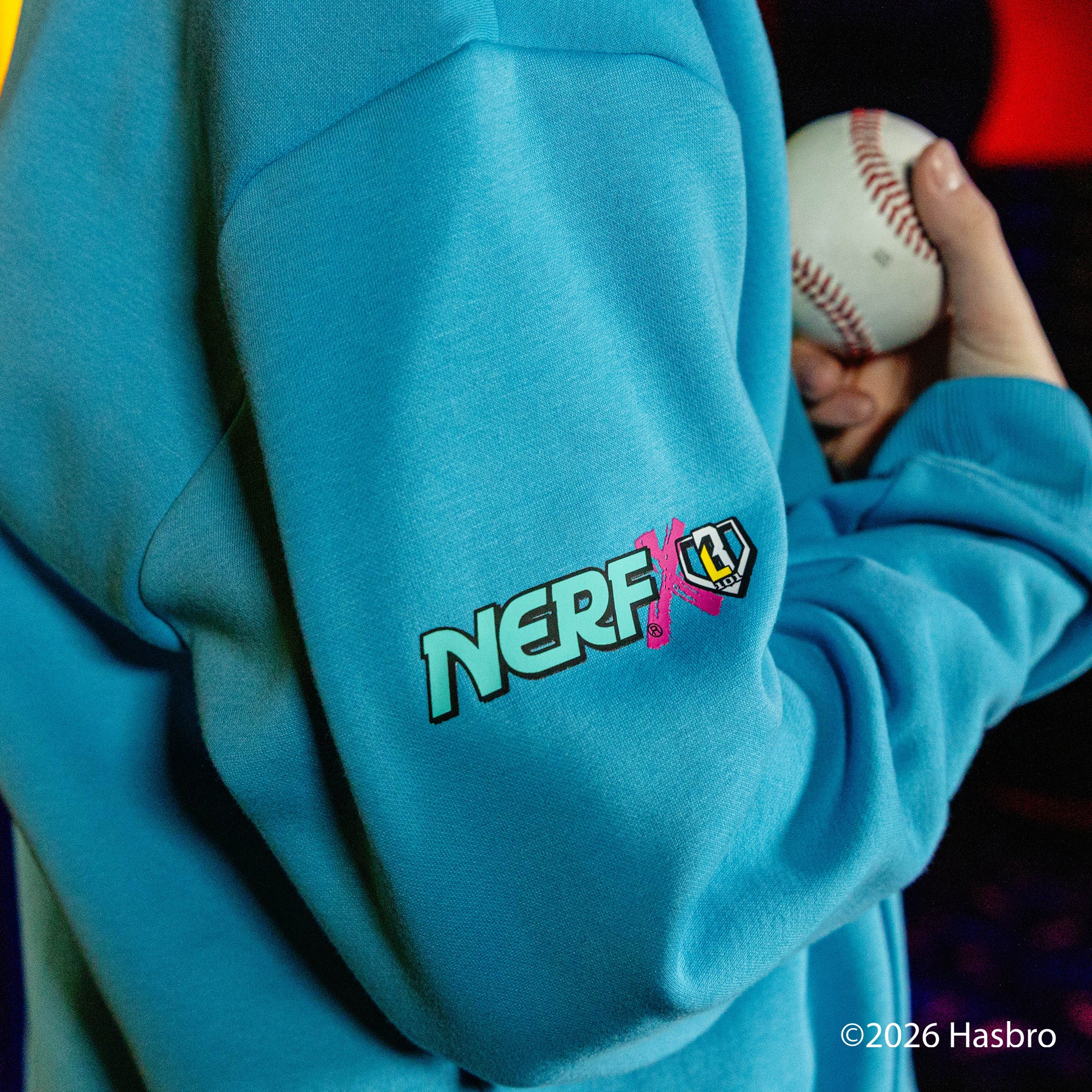Person wearing a blue hoodie with a NERF x BL101 logo, holding a baseball.