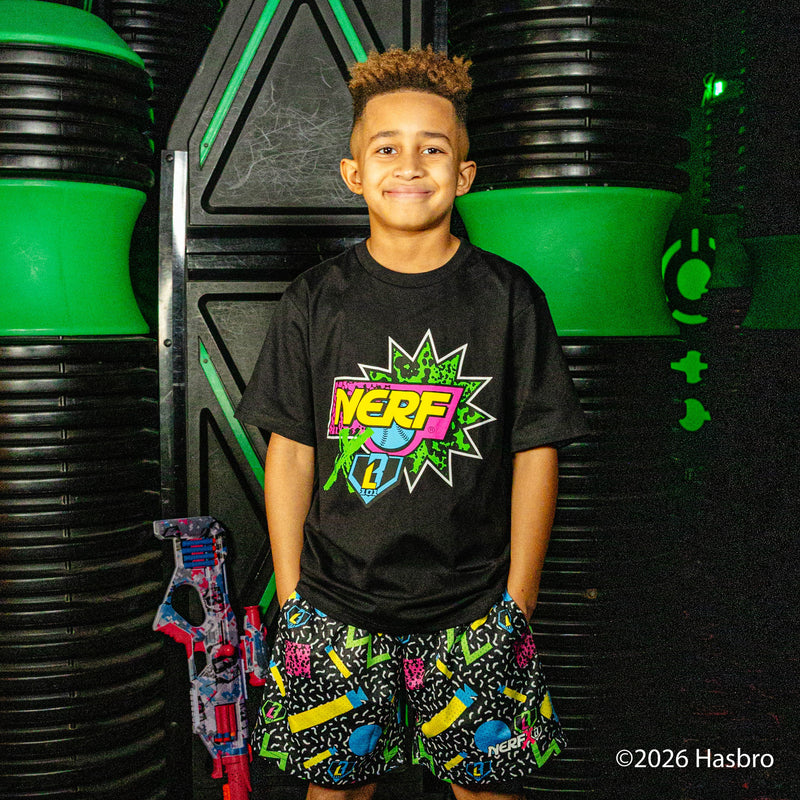 Child wearing a black 'NERF X BL101' t-shirt and colorful shorts standing in front of green and black background