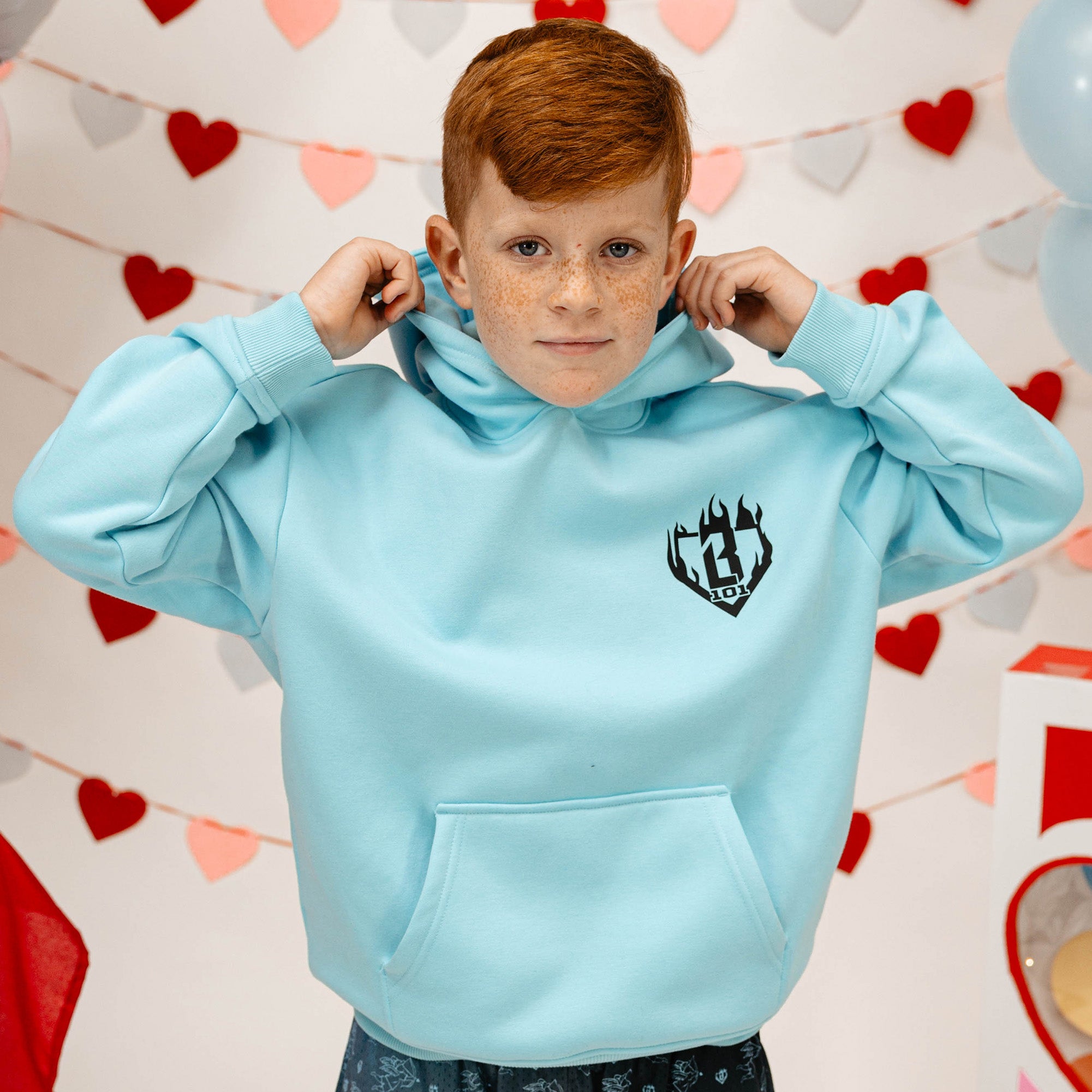 Child wearing a light blue hoodie with a BL101 logo against a heart-themed background