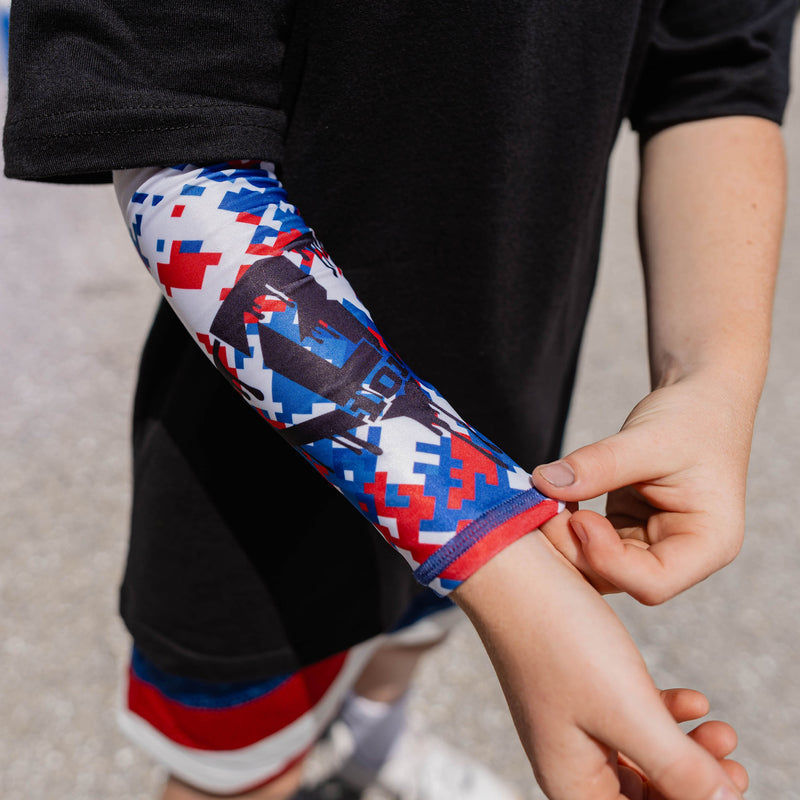 Youth model pulling on red white and blue digital camo arm sleeve showing BL101 logo detail at outdoor event