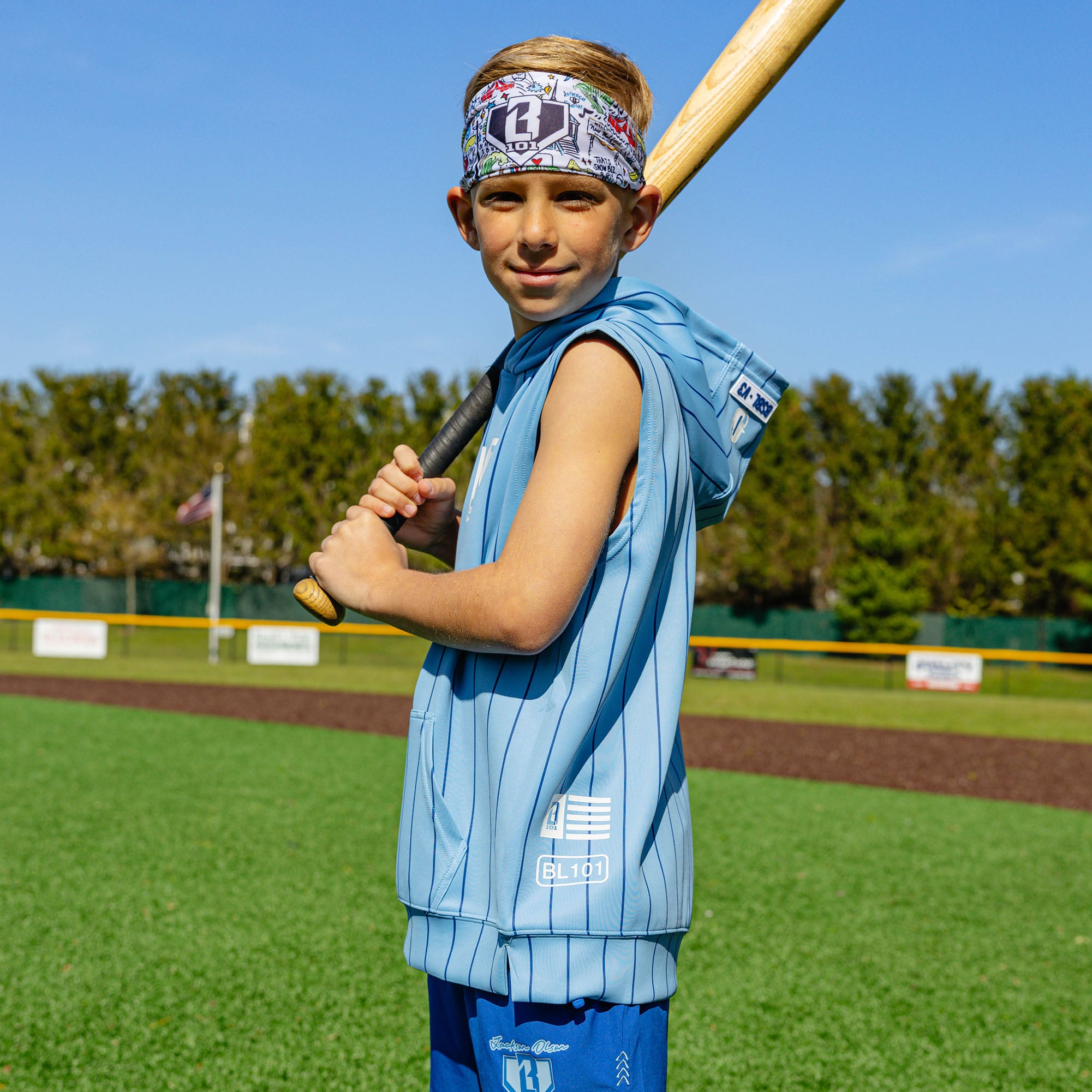 Youth player on a baseball field holding a bat, wearing the Jackson Olson x BL101 white graphic headband