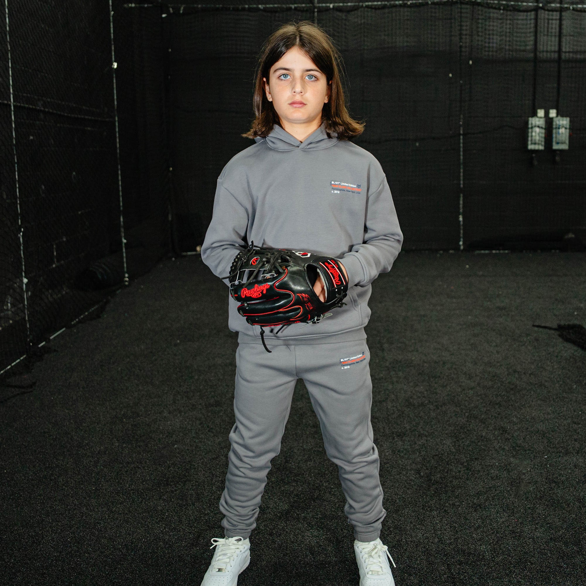 Person wearing a gray hoodie and pants with a glove, standing in an indoor sports facility.