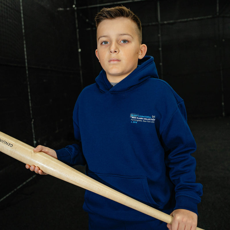 Young boy wearing a blue hoodie holding a baseball bat against a black background