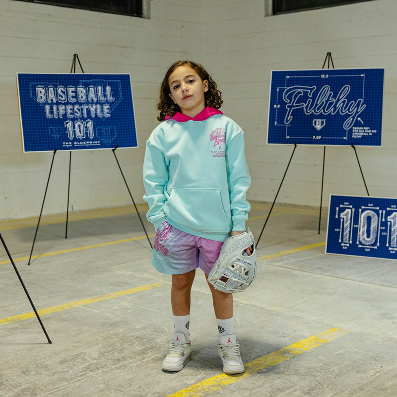 Child in light blue hoodie with pink hood and pink BL101 Ice cream logo with 'Baseball Lifestyle 101' signs in the background