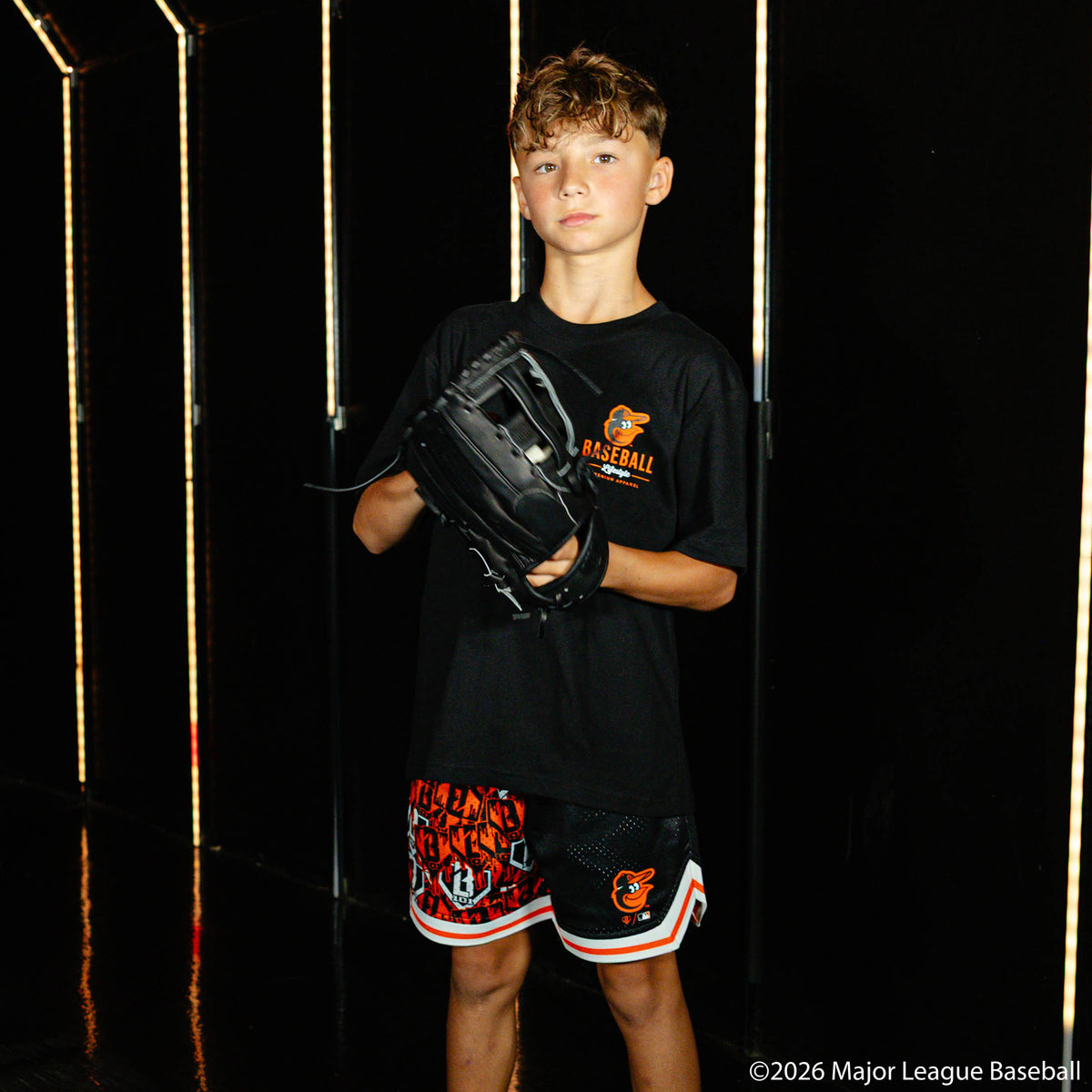 Youth model wearing black youth shorts with "Baltimore Orioles Sticker Court" design
